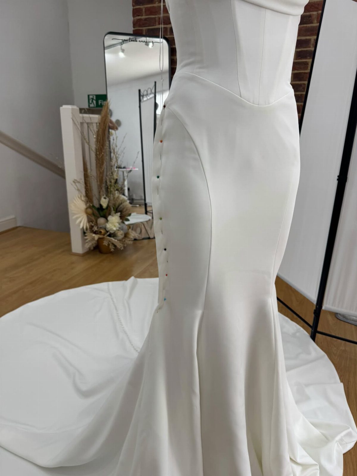 White mermaid wedding dress with back buttons on a mannequin in a studio