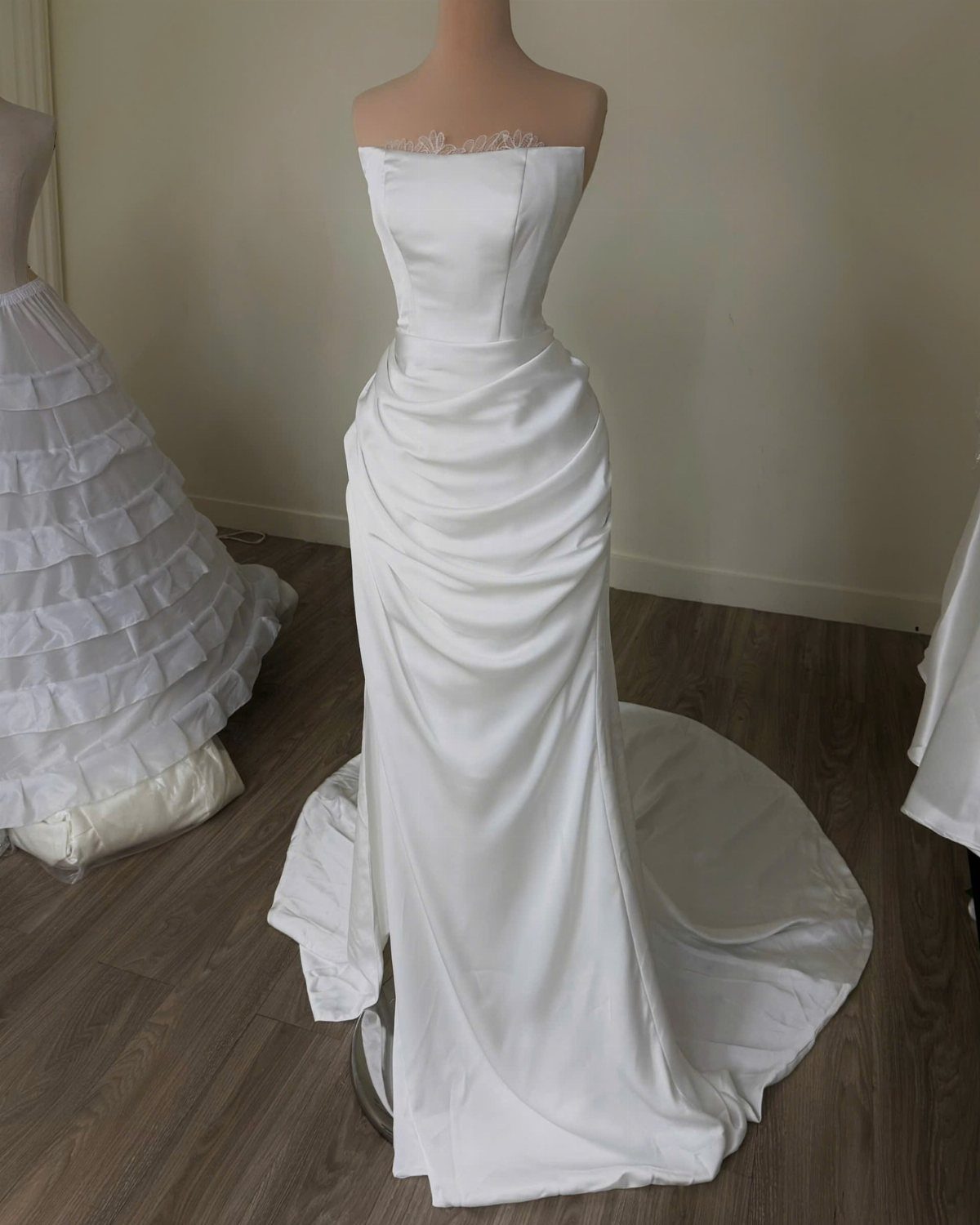White strapless wedding dress with draped skirt on a mannequin in a room