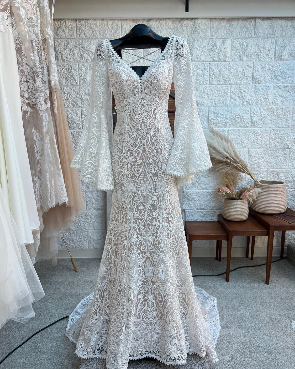 White lace wedding dress with bell sleeves hanging against a white stone wall.