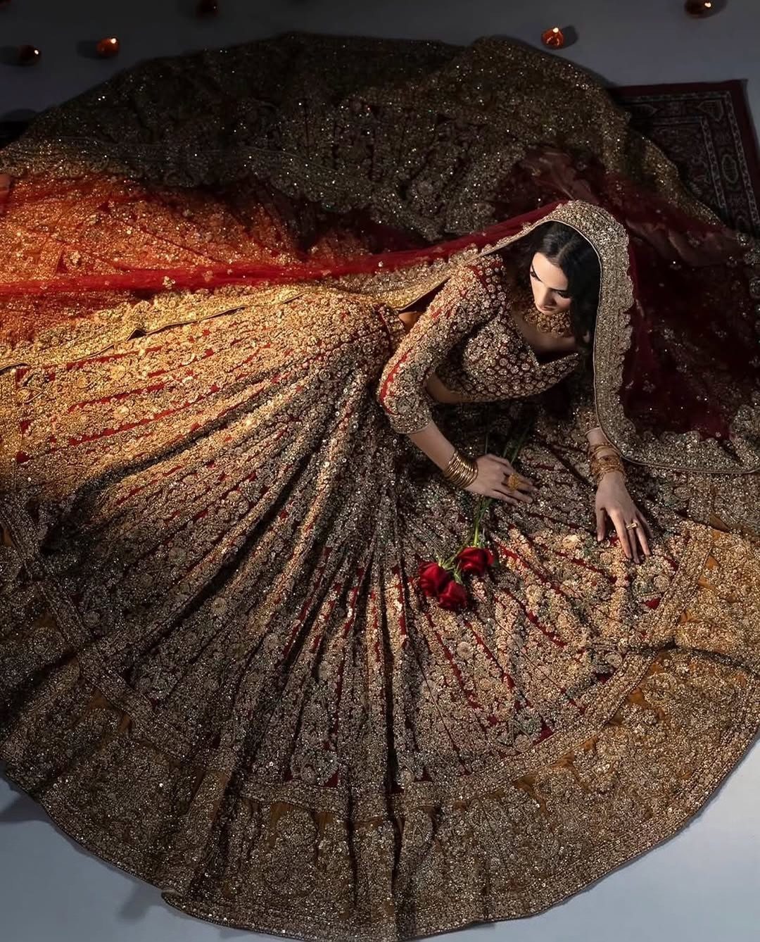 Woman in an ornate gold and red bridal lehenga lying on a dark floor