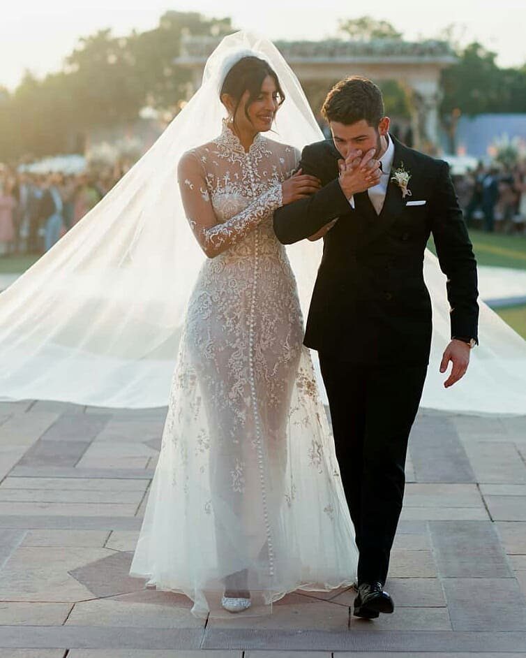 Bride in an intricate white lace wedding dress walking with a groom outdoors.