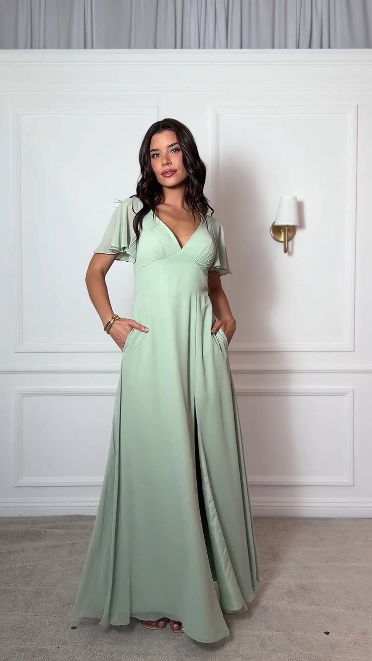 Woman wearing a long dusty sage green bridesmaid dress with flutter sleeves and pockets.