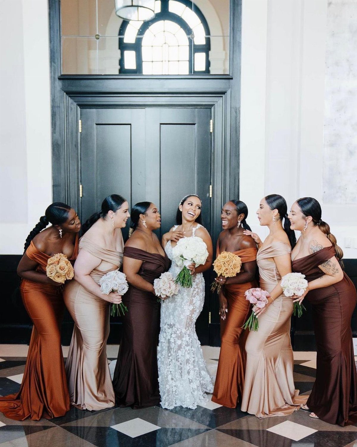 Bride and bridesmaids in earth-toned off-the-shoulder gowns posing in a bright hall