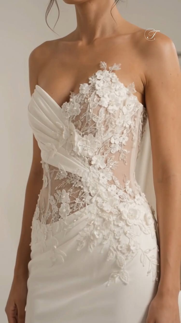 White strapless wedding dress with 3D floral lace appliqués and draped fabric details.