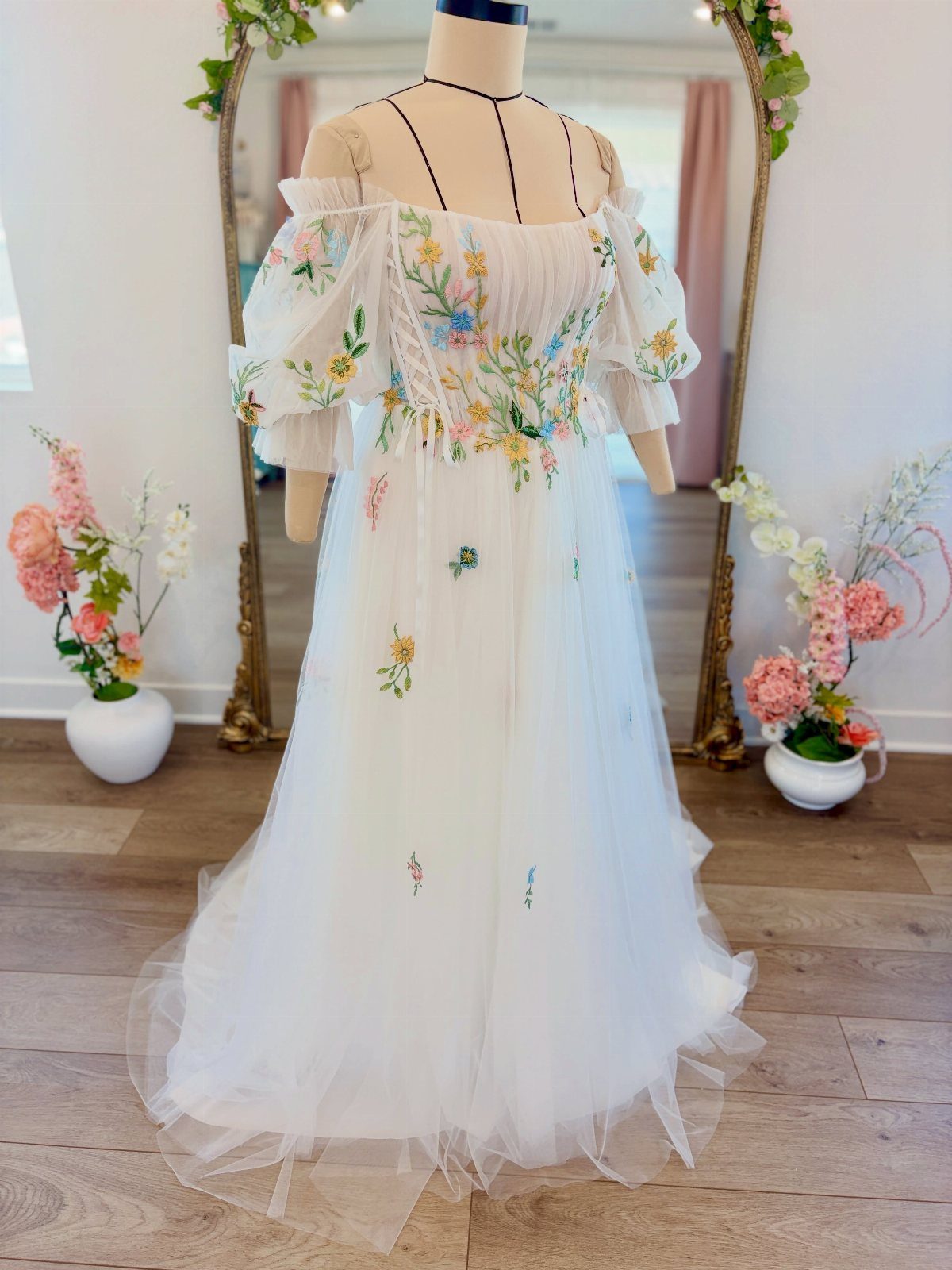 White wedding dress on a mannequin with colorful floral embroidery and tulle skirt.