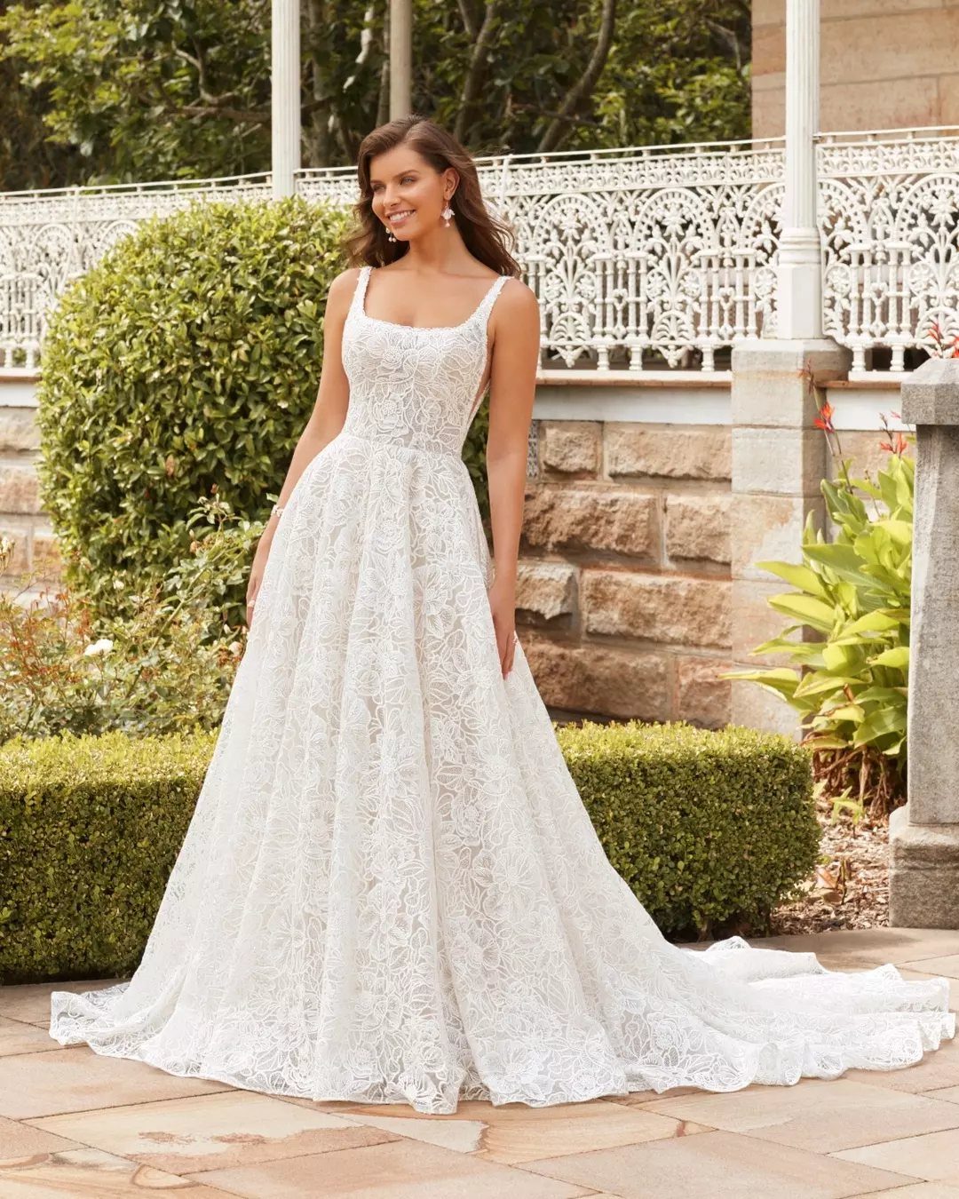 Woman in a white floral lace wedding dress standing on a stone patio.