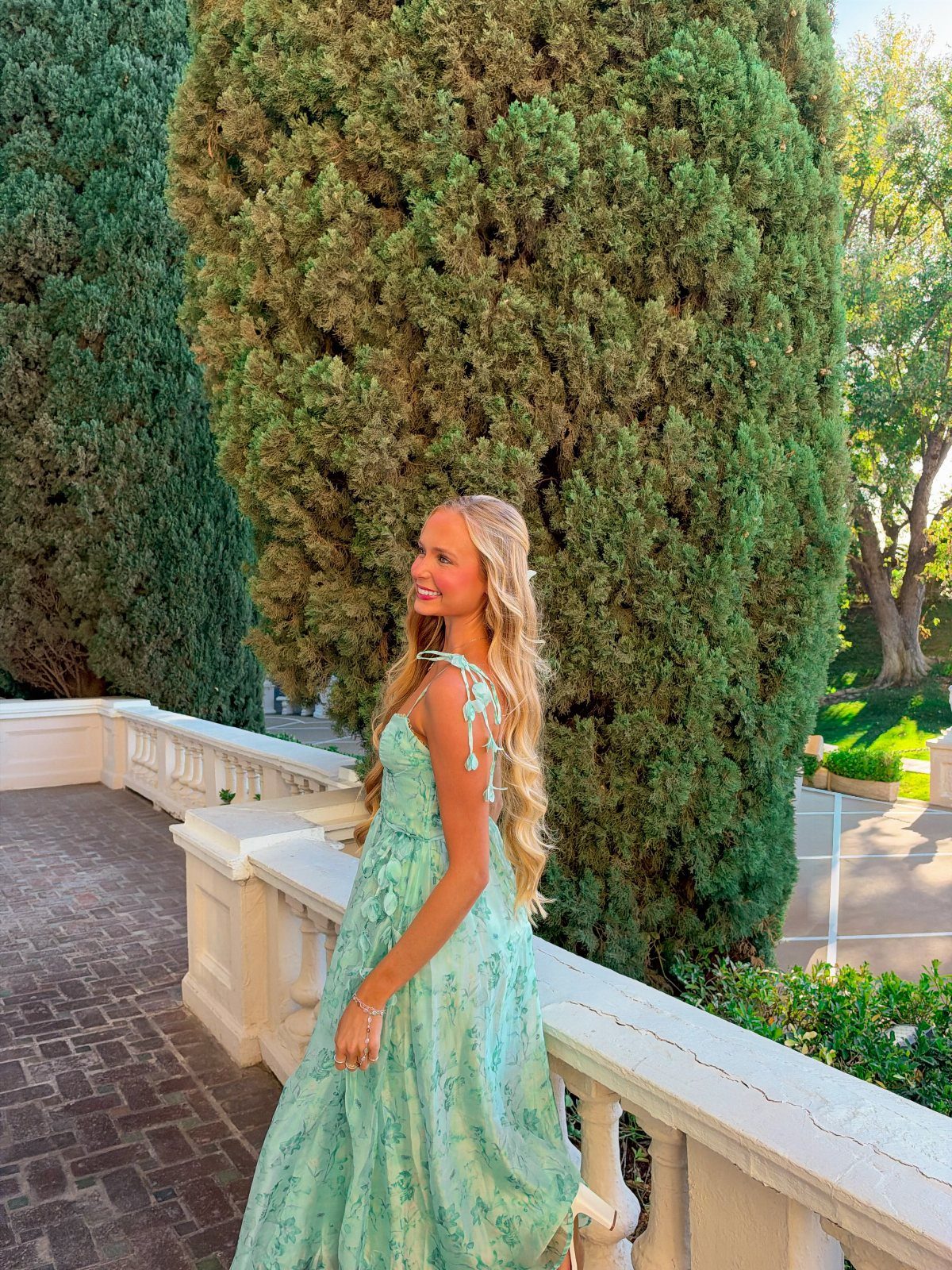Woman in a light green floral maxi dress posing on a stone balcony