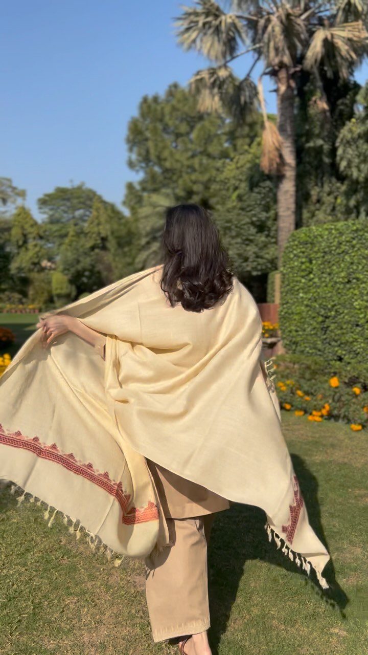 Woman in cream outfit and embroidered shawl standing in a sunny green garden