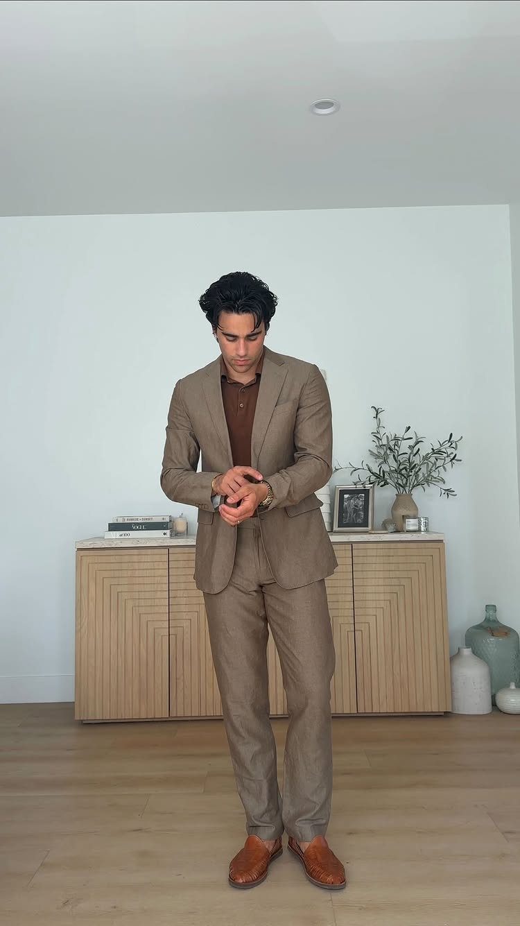 Man in a tan suit and brown shirt posing in a modern room