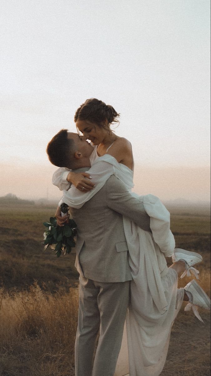 Groom lifting bride in a field while holding a white floral wedding bouquet