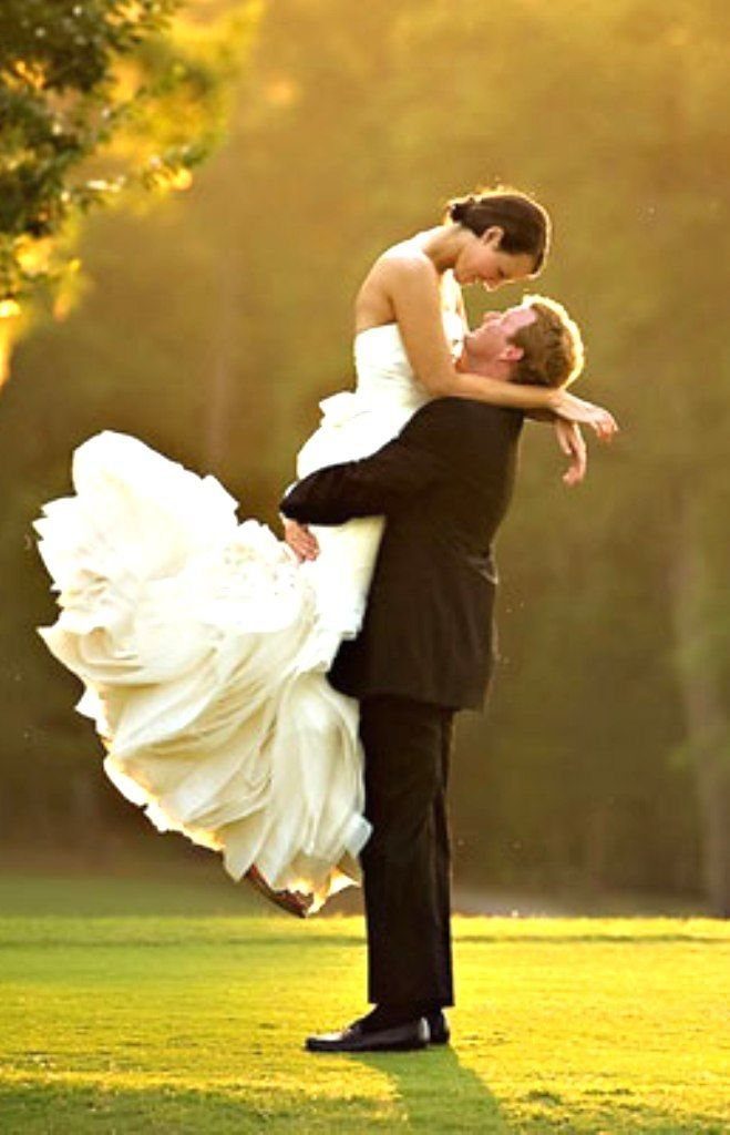 Groom lifting bride in a white wedding dress while dancing outdoors at sunset