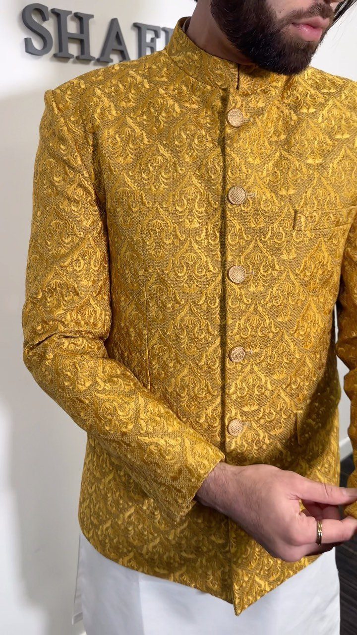 Man wearing a gold patterned brocade jacket with a mandarin collar and white trousers.