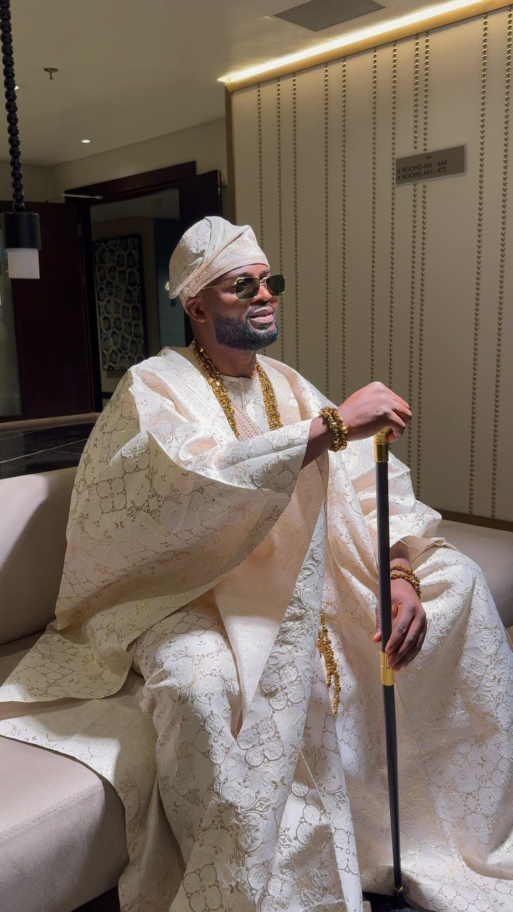 Man in traditional cream Agbada and fila hat sitting on a sofa