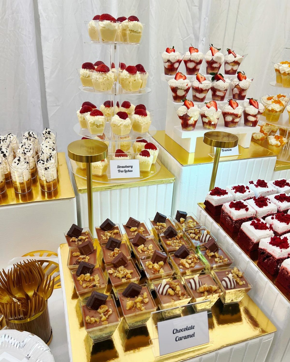 Miniature dessert buffet with chocolate, red velvet, and strawberry treats on gold stands.