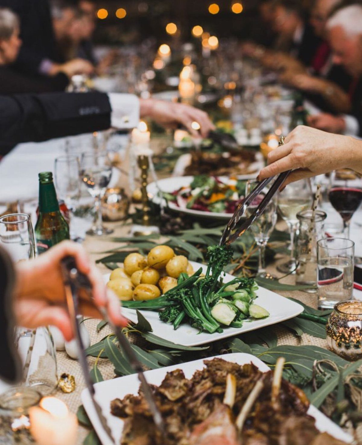 Platters of roasted meat and vegetables on a long table with guests serving.