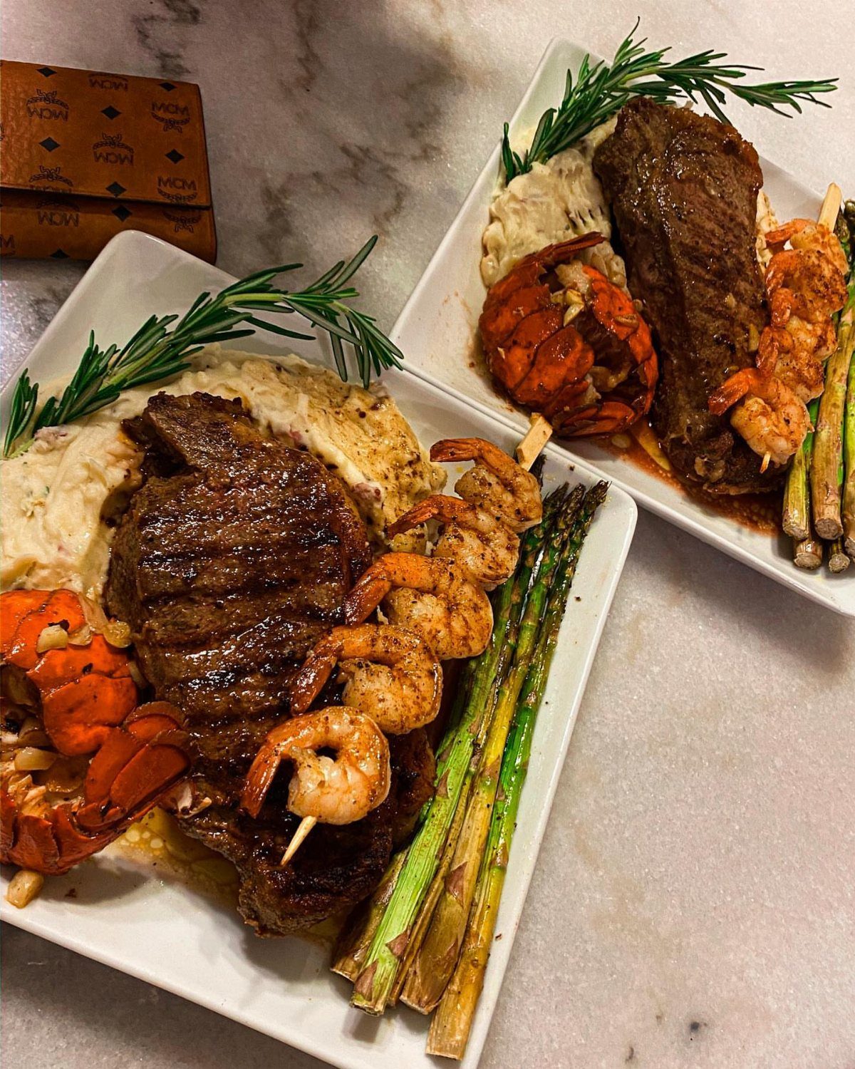 Grilled steak and lobster tail with shrimp and asparagus on white plates.