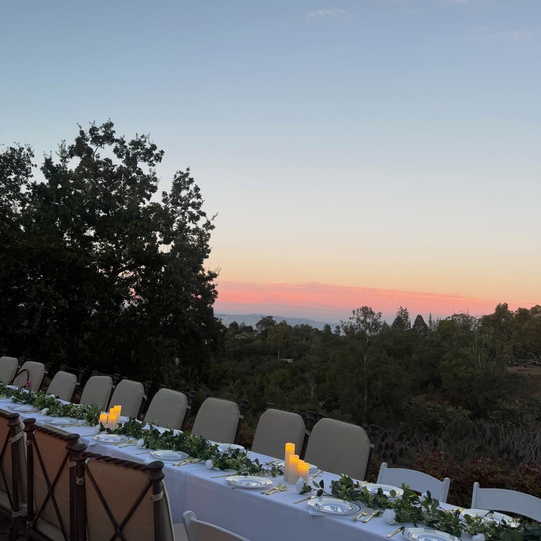 Long outdoor dining table with white linens and greenery at sunset