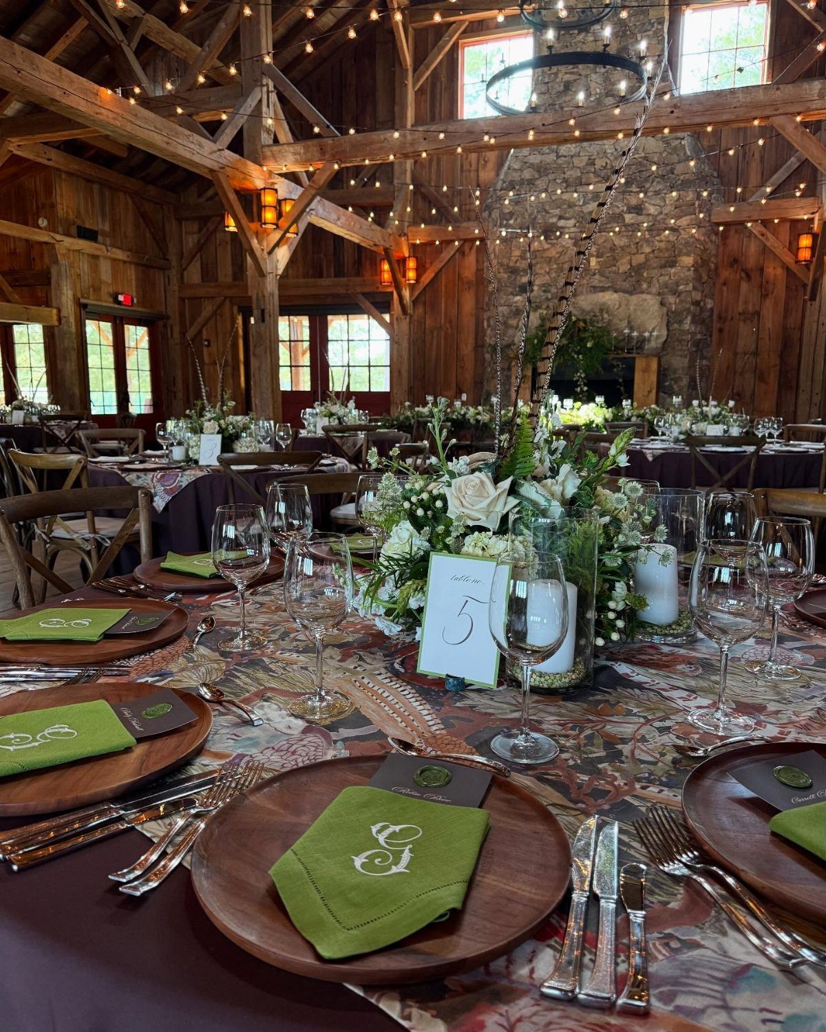 Rustic barn dinner table set with wooden plates, green napkins, and white flowers.