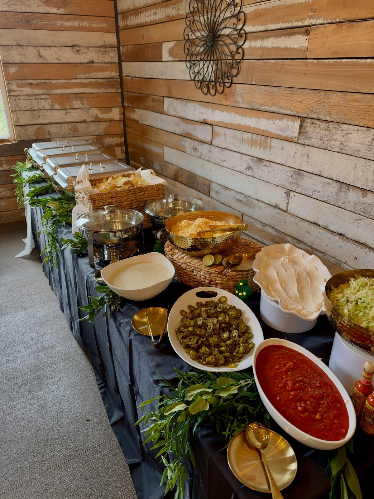 Taco bar buffet with salsa, olives, and tortillas on a black tablecloth.