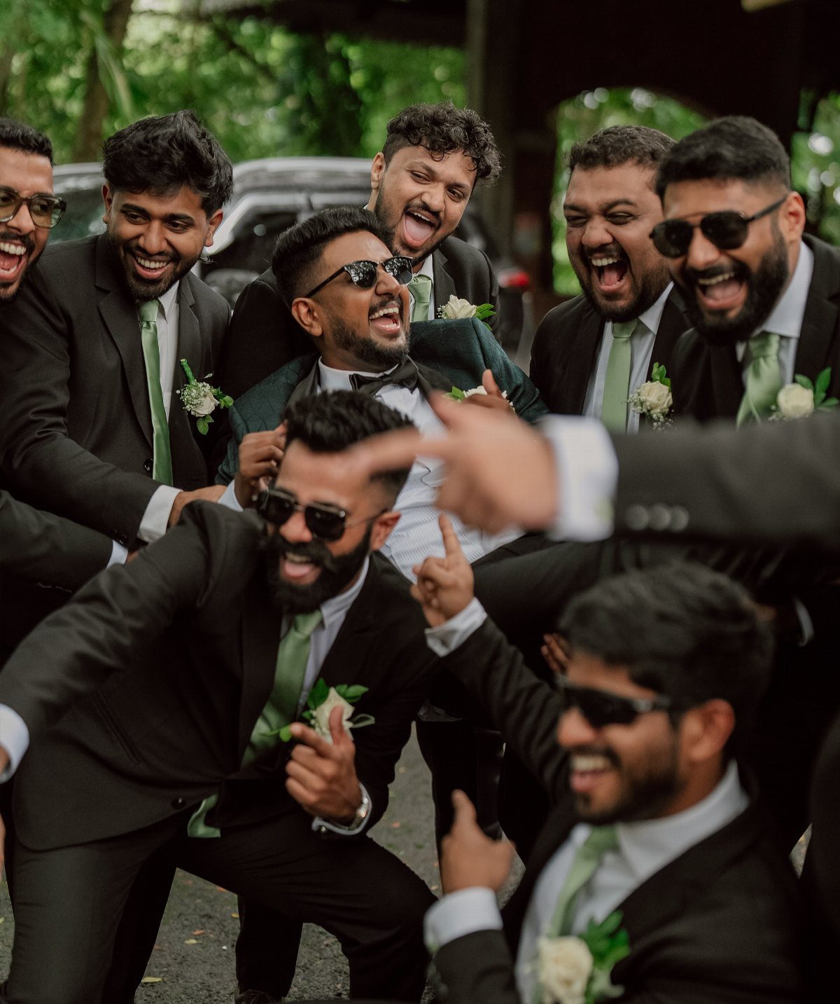 Groomsmen in black suits and green ties posing like a rock band outdoors.