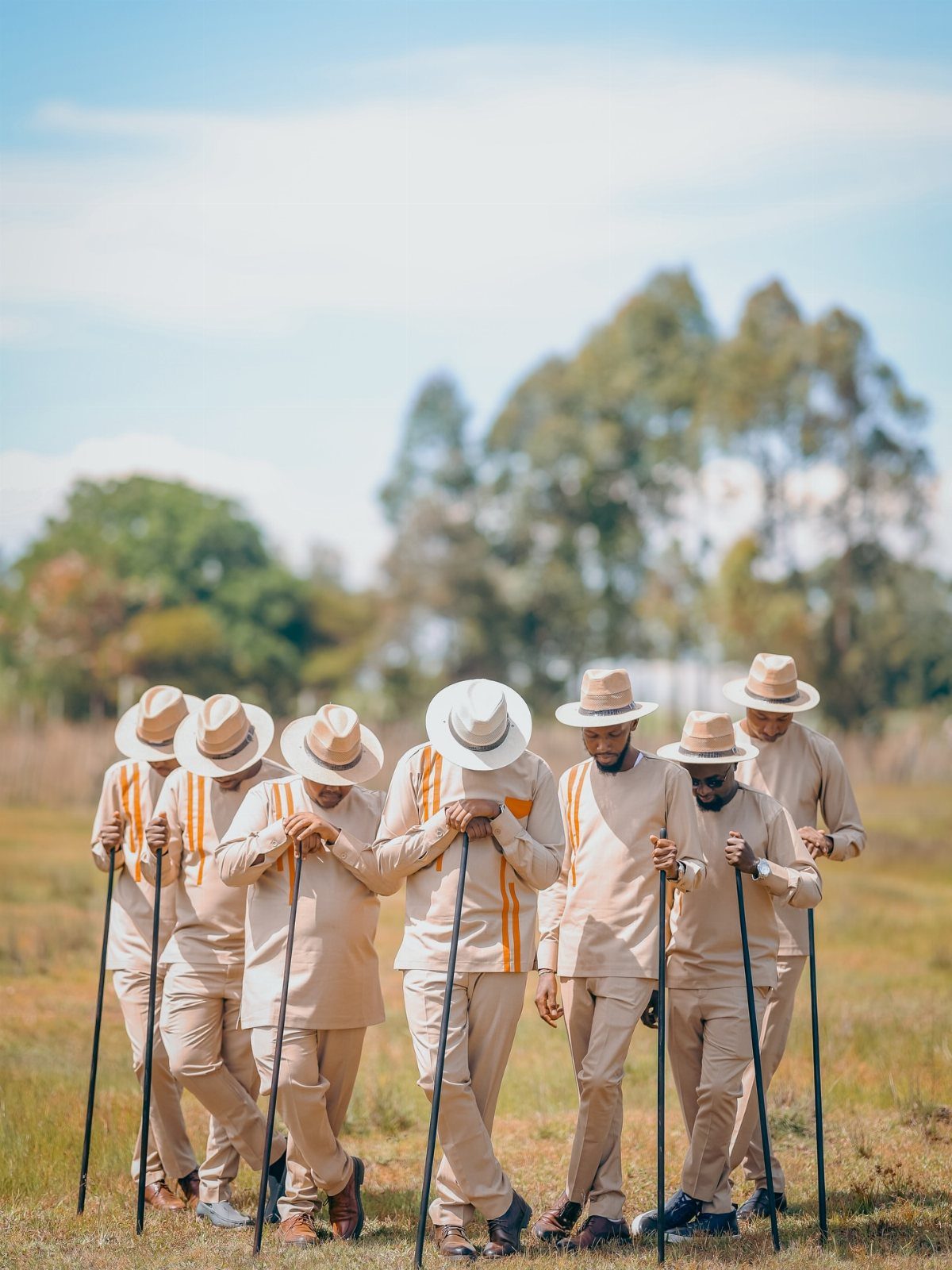 Seven men in beige suits and hats posing with golf clubs in a field.