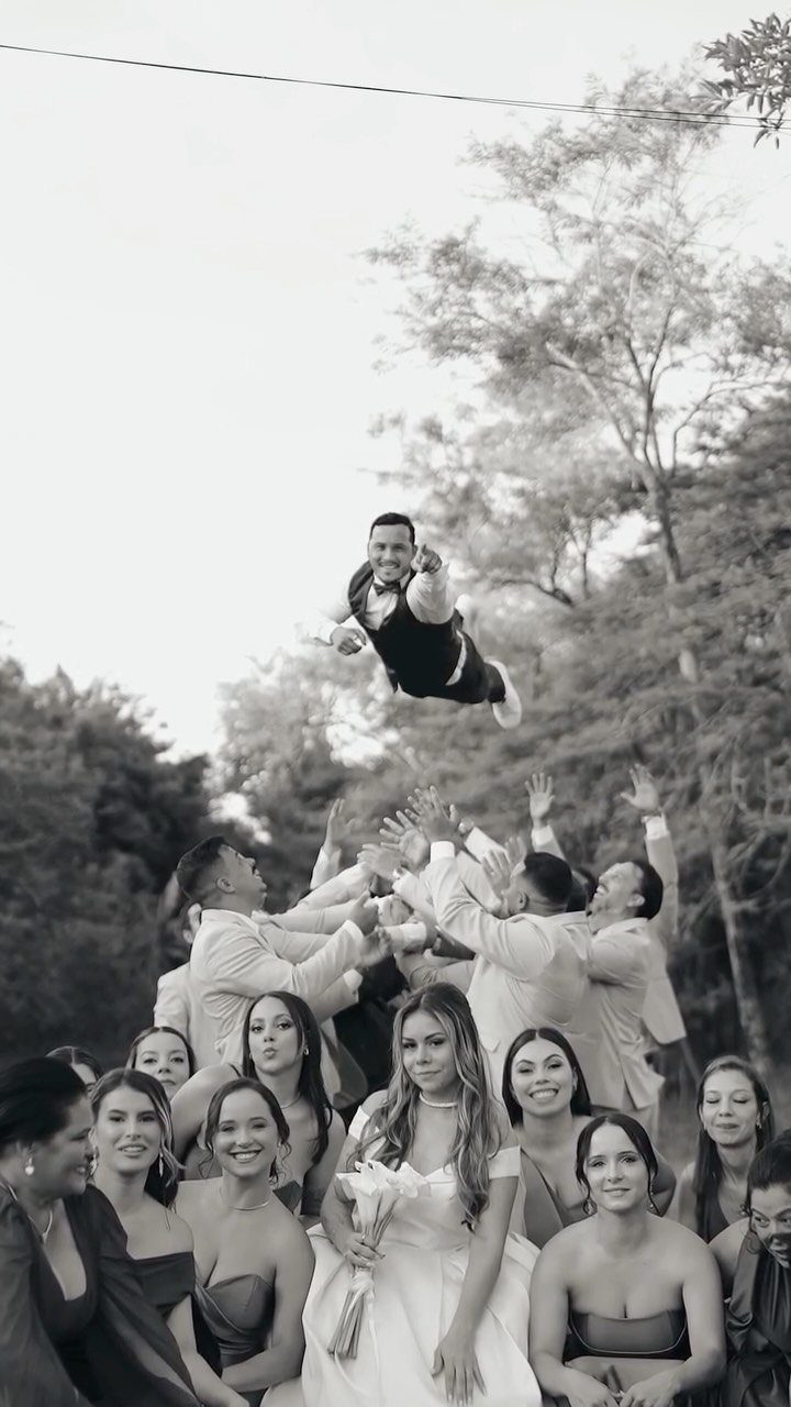 Groom tossed in the air by groomsmen with bride and bridesmaids watching below.