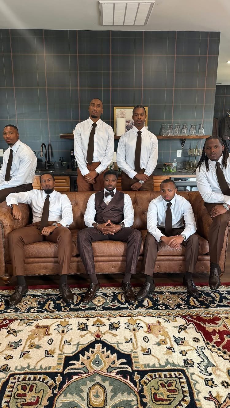 Groom and groomsmen posing together in white shirts and brown trousers indoors.