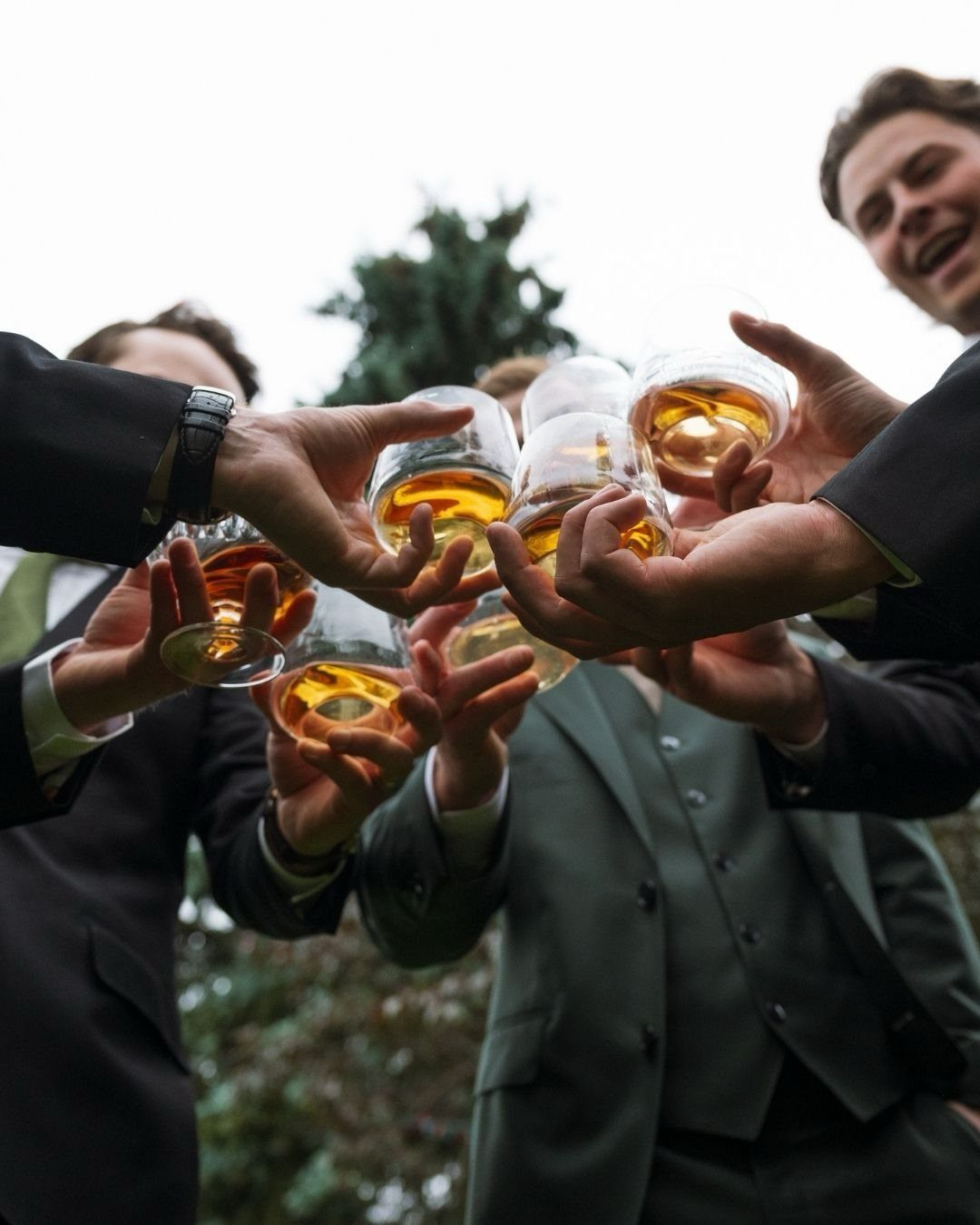 Men in suits clinking glasses of amber liquid during a celebratory outdoor toast.