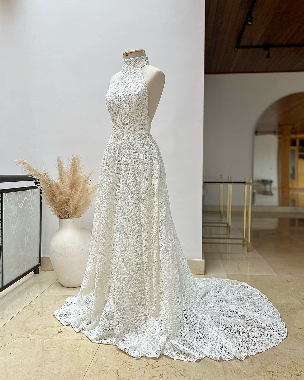 White lace halter wedding dress on a mannequin with a long flowing train.