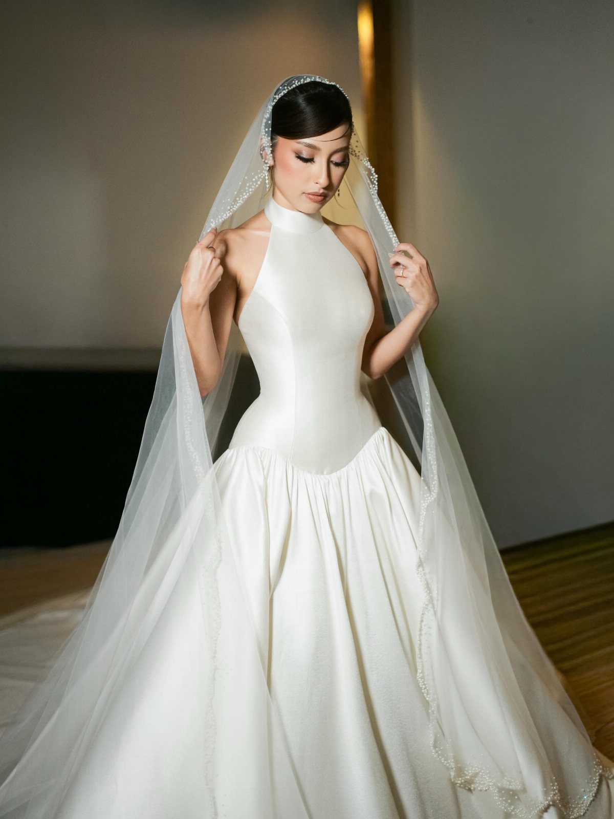 Woman in a white satin halter wedding dress with a long sheer veil.