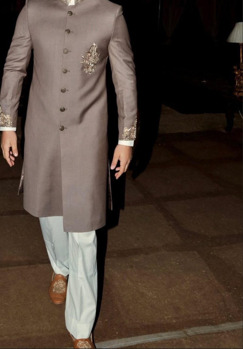 Man wearing a taupe Achkan jacket with silver embroidery and white trousers.