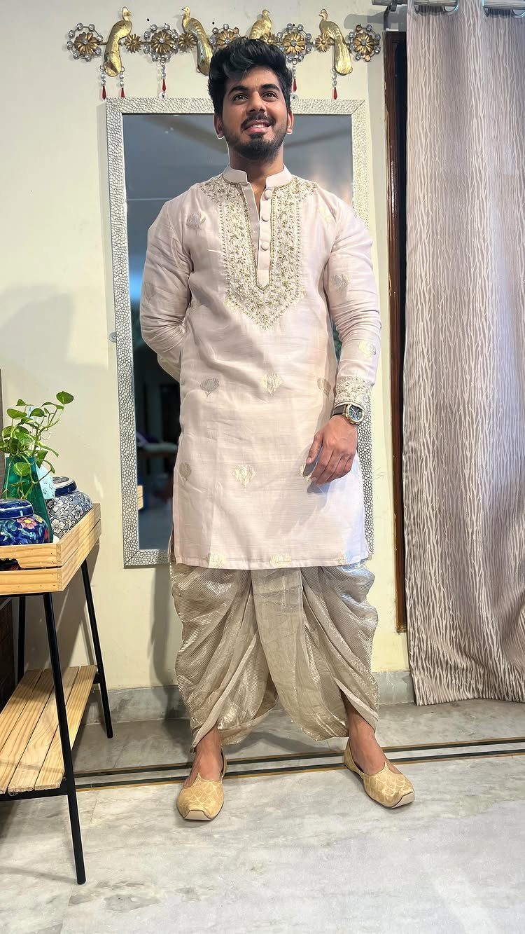 Man wearing a light pink embroidered kurta and gold draped dhoti pants.