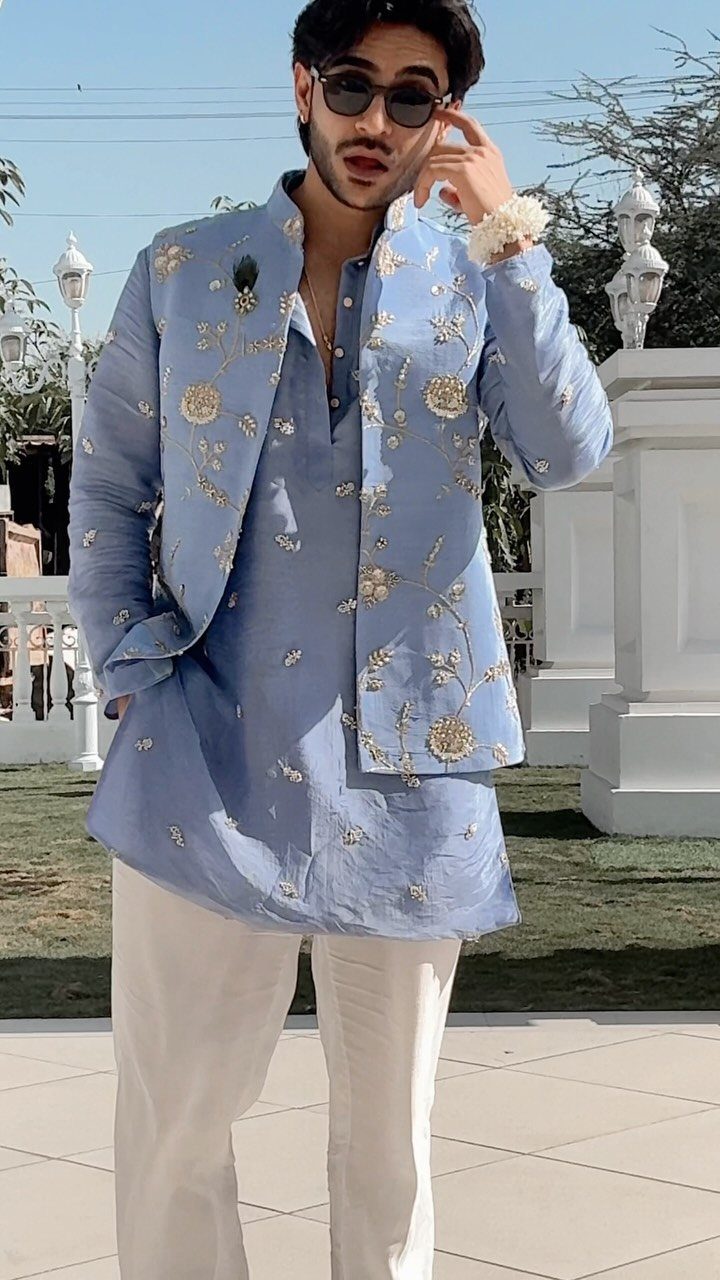 Man in light blue embroidered Indian wedding attire with white trousers and sunglasses.