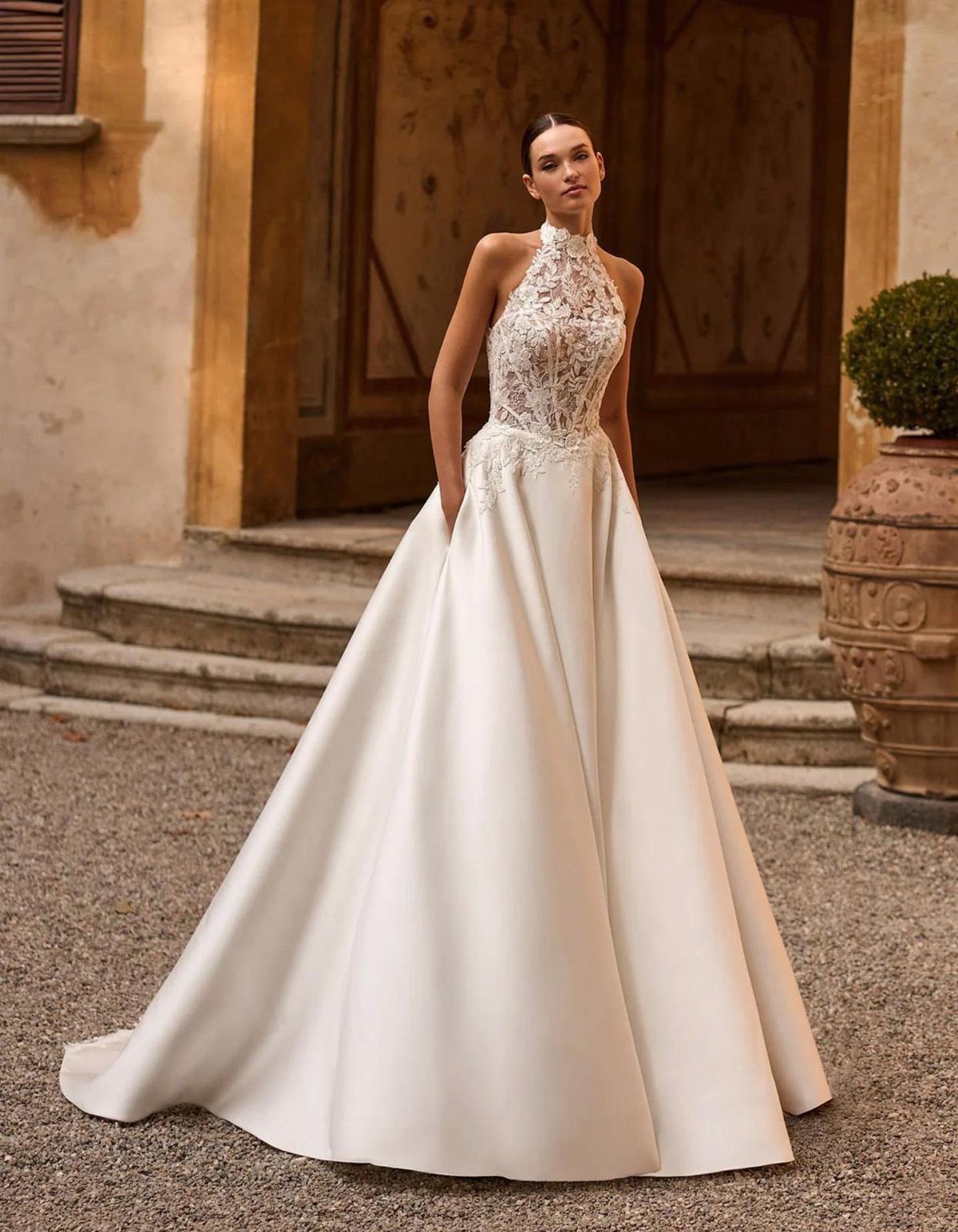 Woman in a white lace and satin wedding dress standing before a stone building