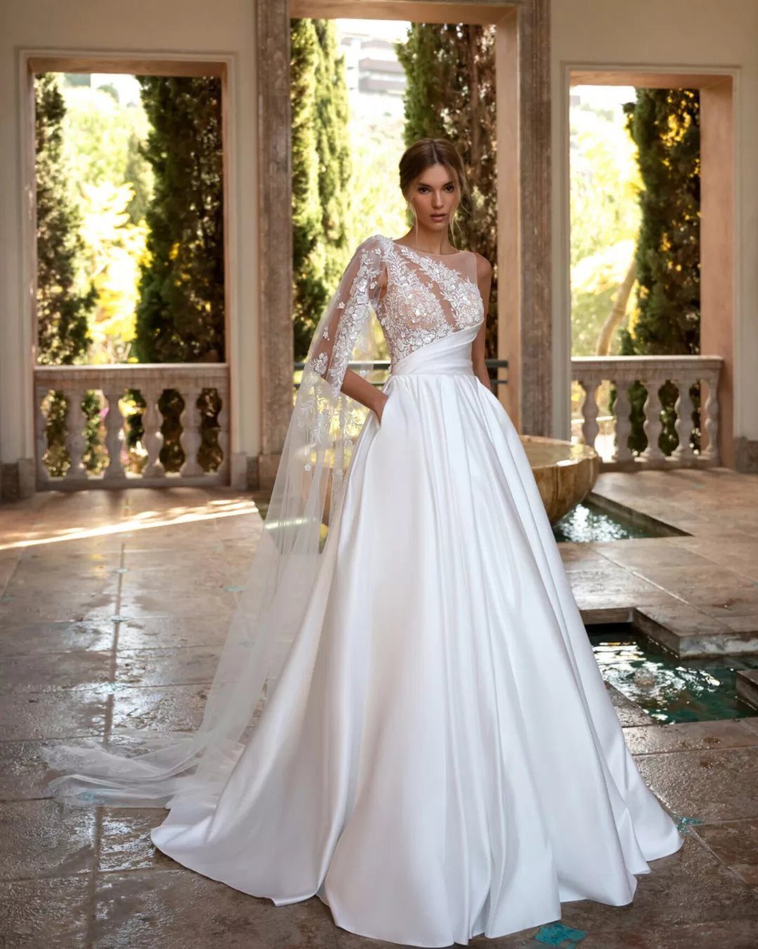 Woman in a white one-shoulder lace and satin wedding dress in a stone courtyard