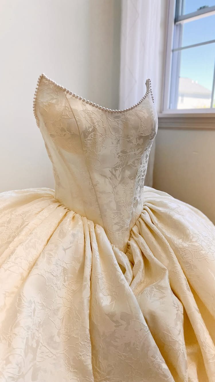Cream jacquard ball gown with a structured bodice and voluminous floral textured skirt.