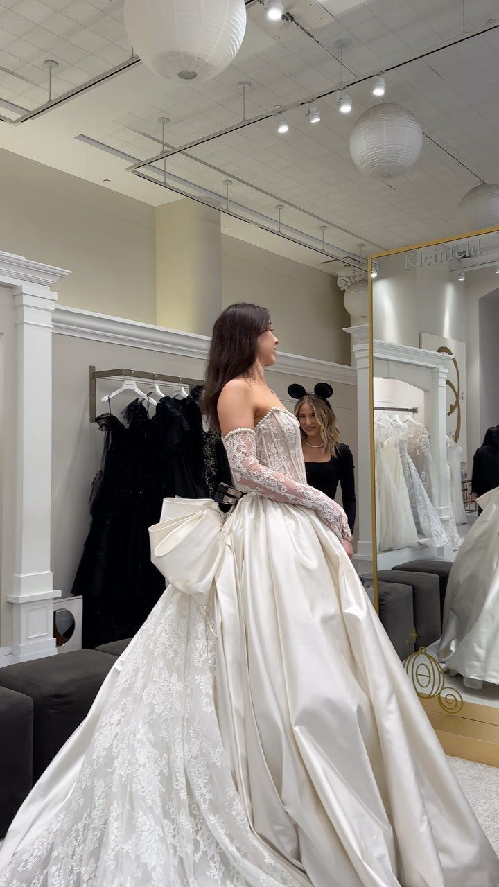 Woman wearing a voluminous white ballgown wedding dress in a bridal salon setting.