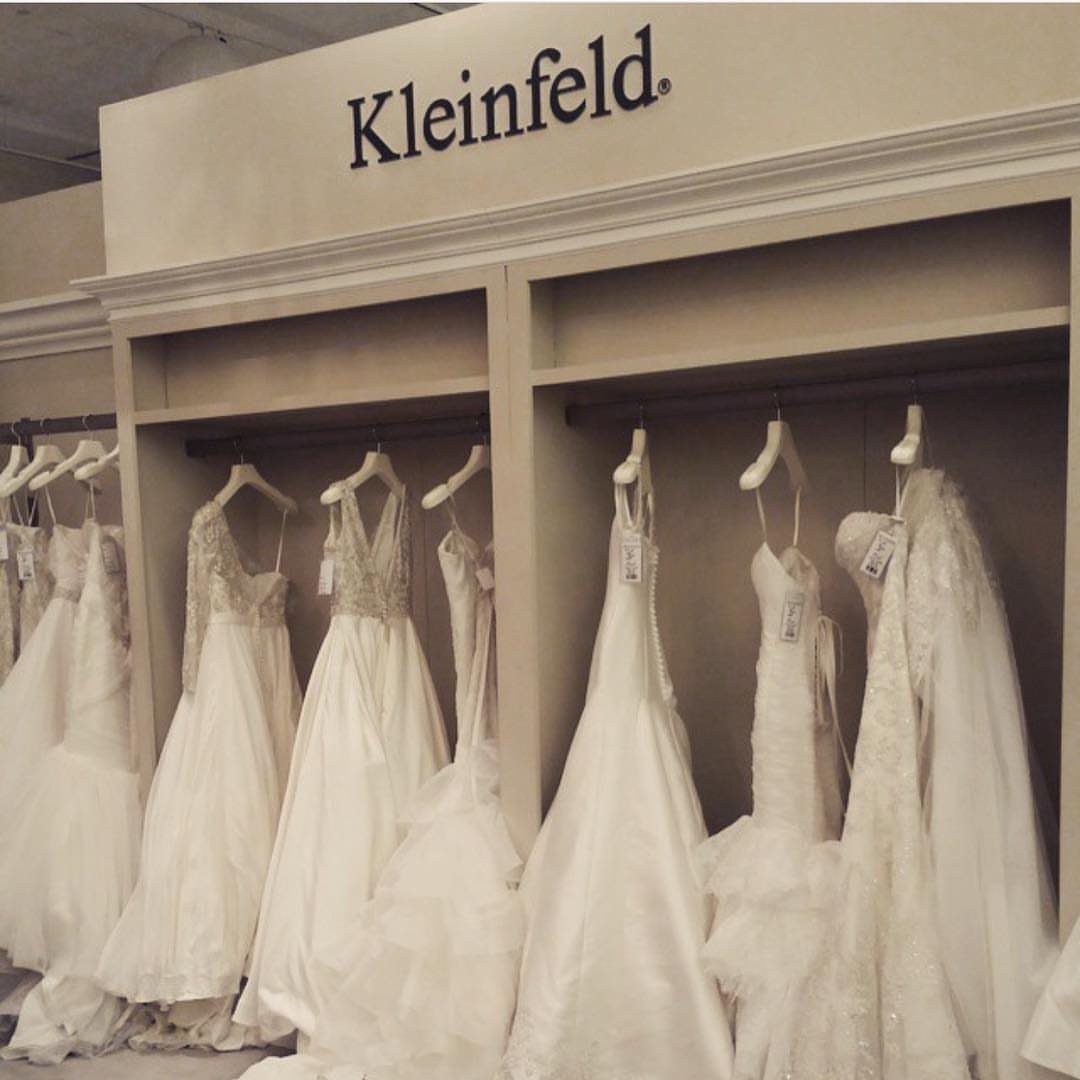 White wedding dresses hanging in a row under a Kleinfeld bridal store sign.