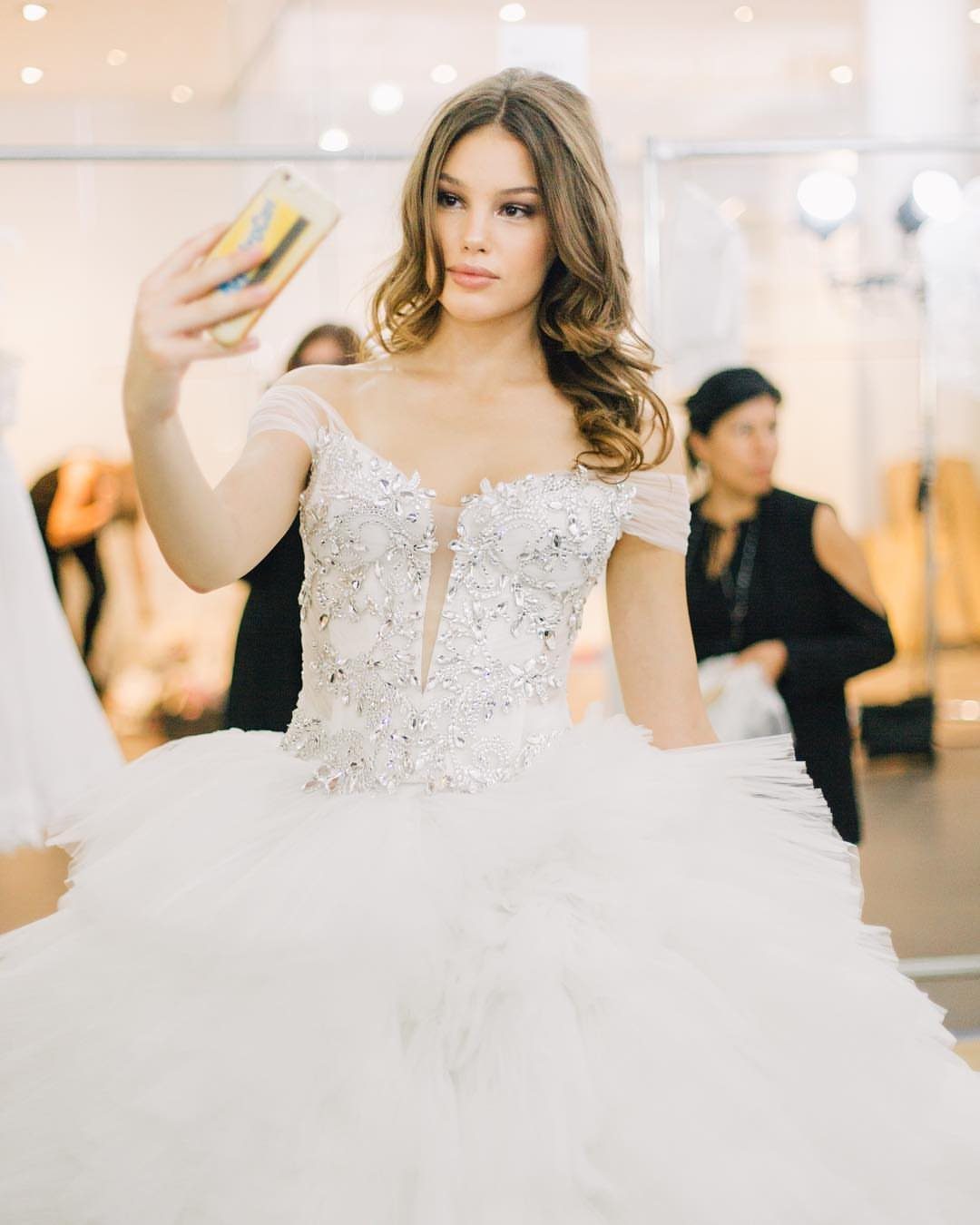 Woman in an ornate white beaded wedding dress taking a selfie in a salon.