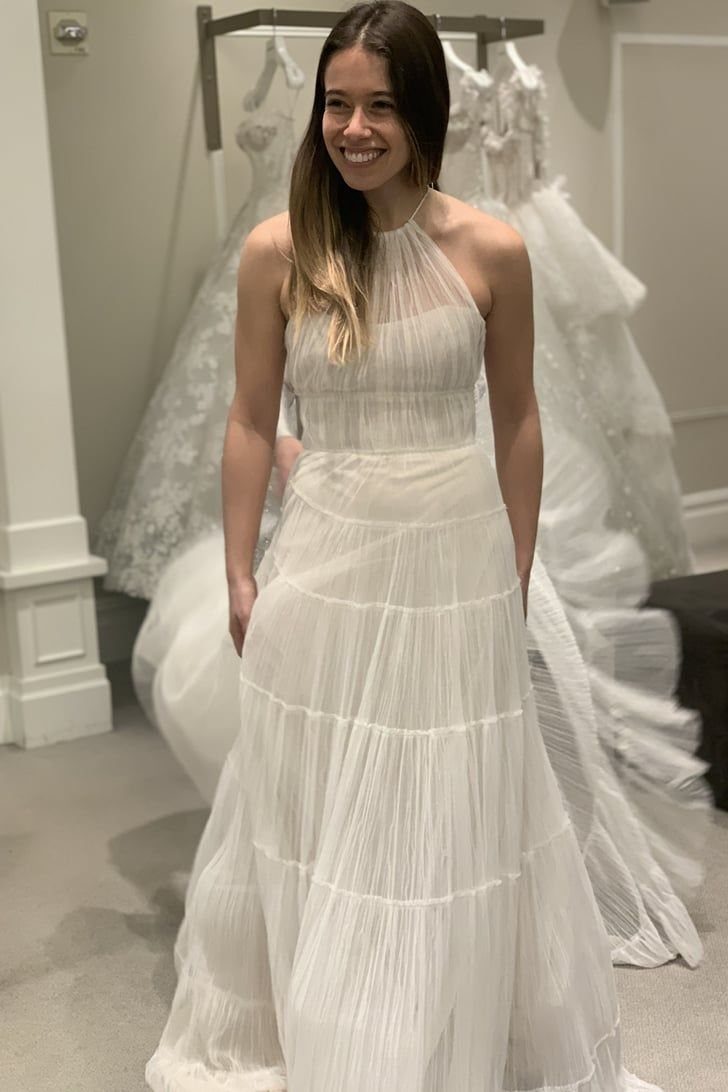 Woman smiling in a tiered white wedding dress inside a bridal salon.