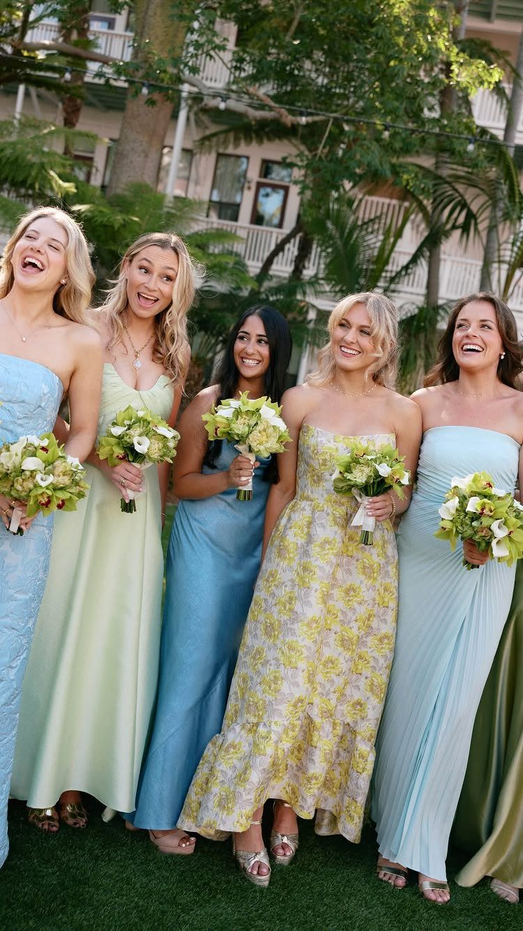 Five bridesmaids in mismatched light blue, yellow, and floral dresses holding white bouquets.