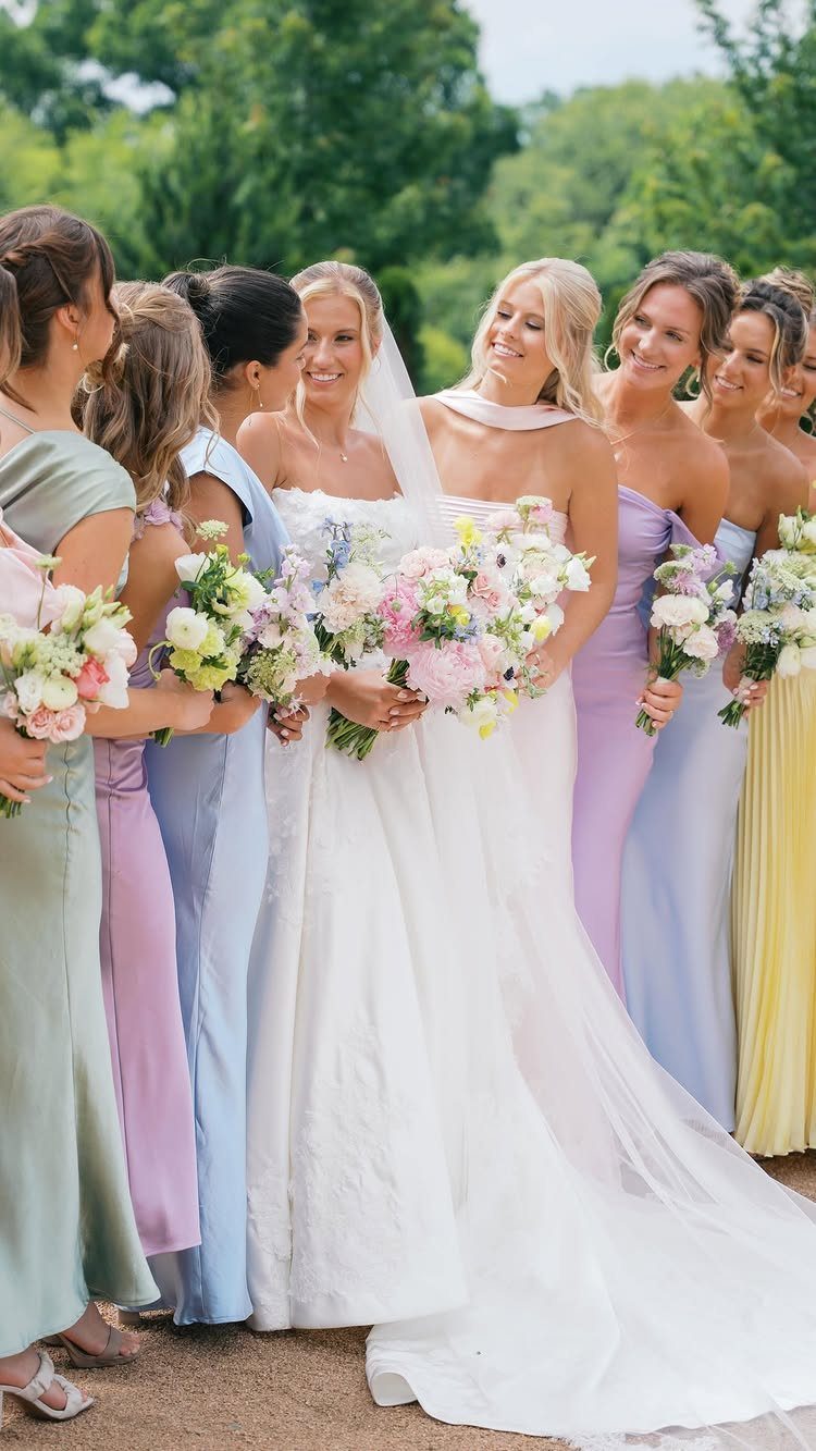 Bride in white gown surrounded by bridesmaids in mismatched pastel colored dresses.