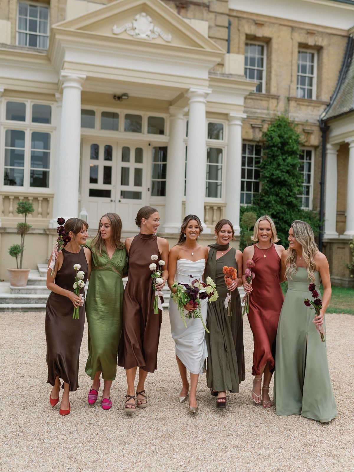Seven bridesmaids in different styles and shades of green and brown dresses.