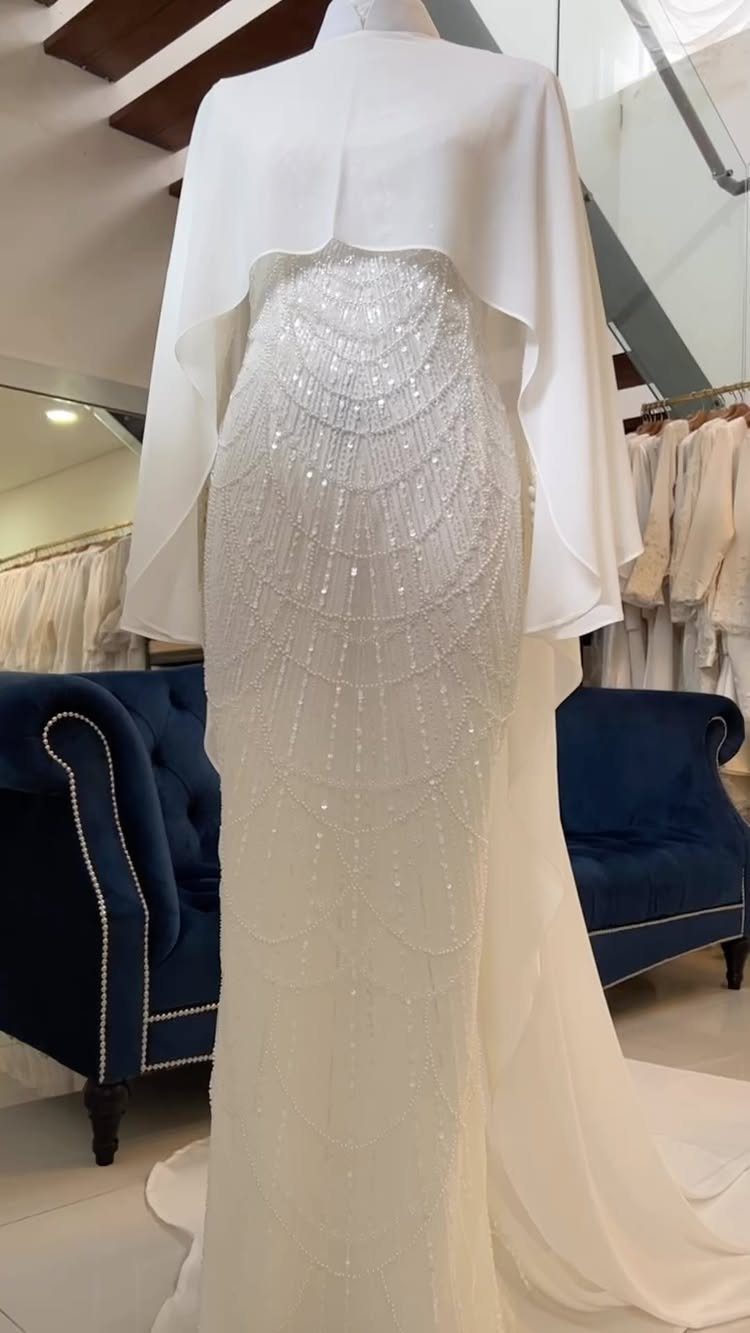 White wedding gown on a mannequin with embroidered sequin patterns and a cape.