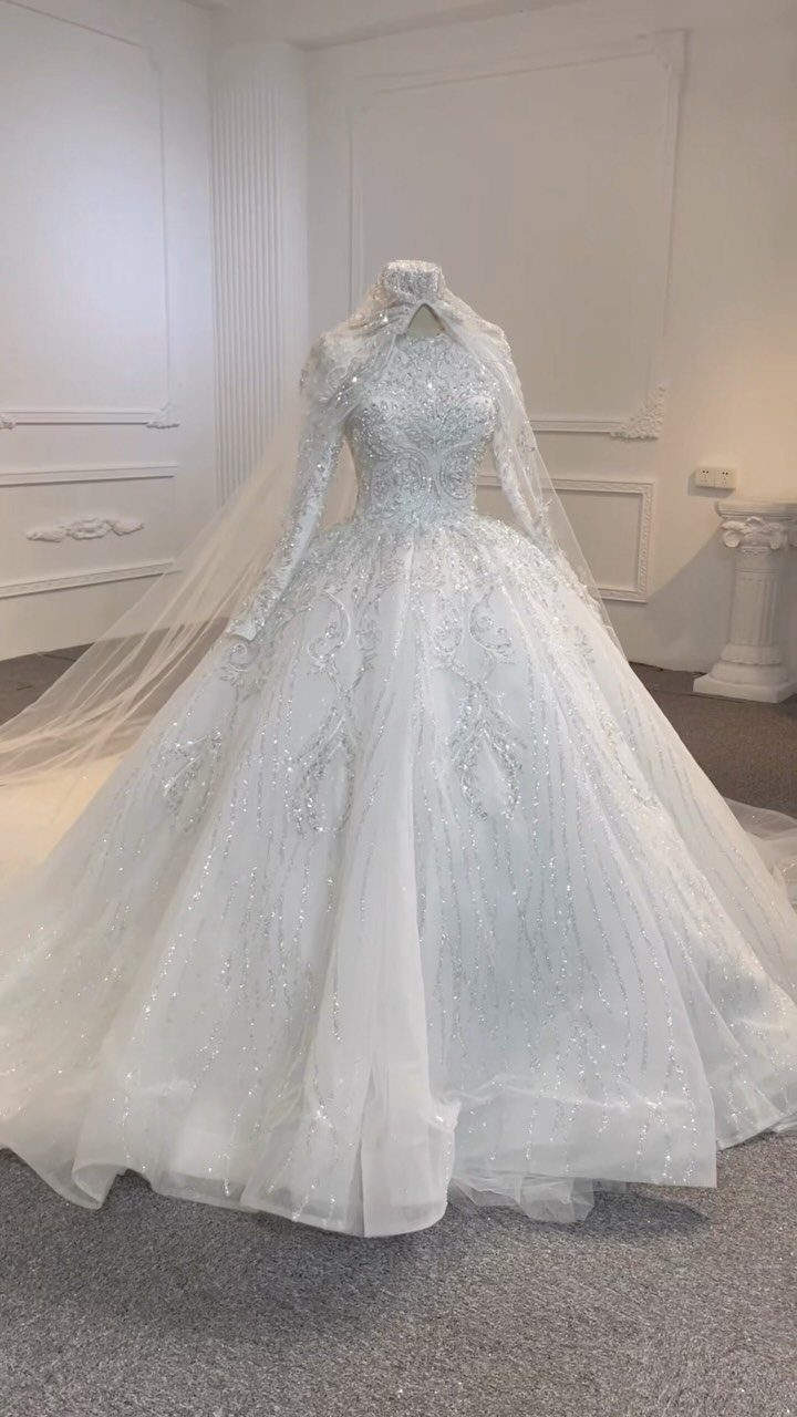 White long-sleeved wedding gown with sparkling embroidery and veil on a mannequin