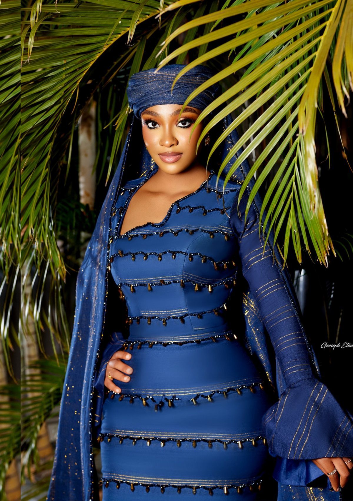 Woman in navy blue traditional Nigerian bridal attire with matching headtie and veil.