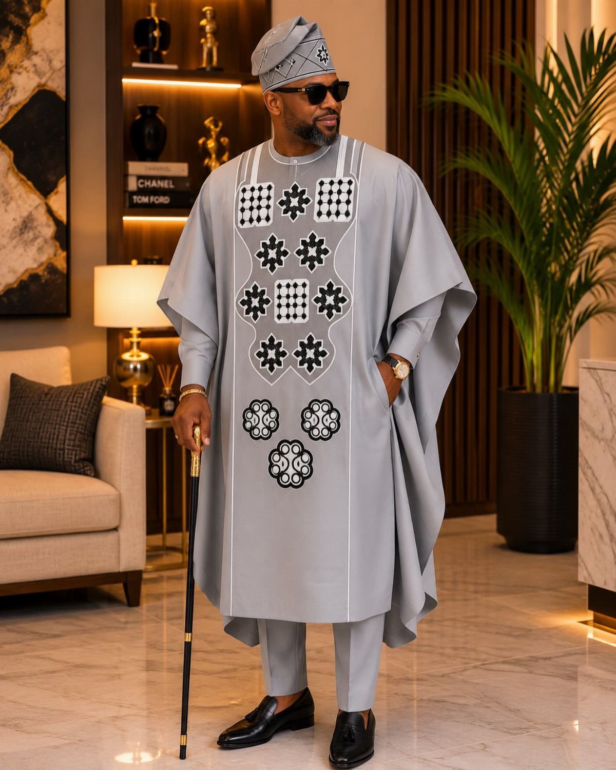 Man in grey traditional Nigerian agbada with embroidery, fila cap, and walking stick.