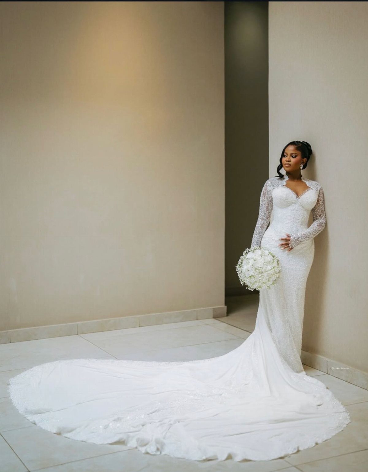 Woman in a white lace wedding dress with a long train holding flowers.
