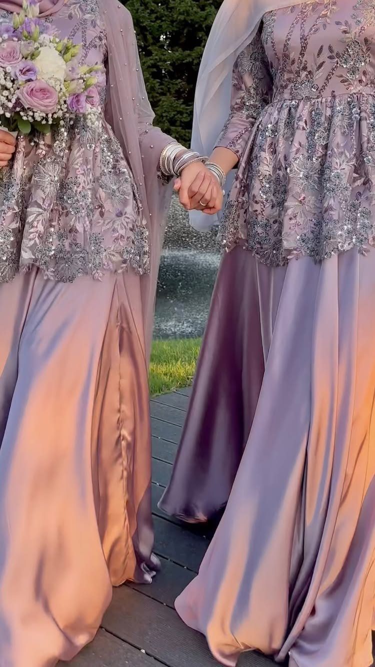 Two people in periwinkle purple embroidered bridesmaid dresses holding hands outdoors.