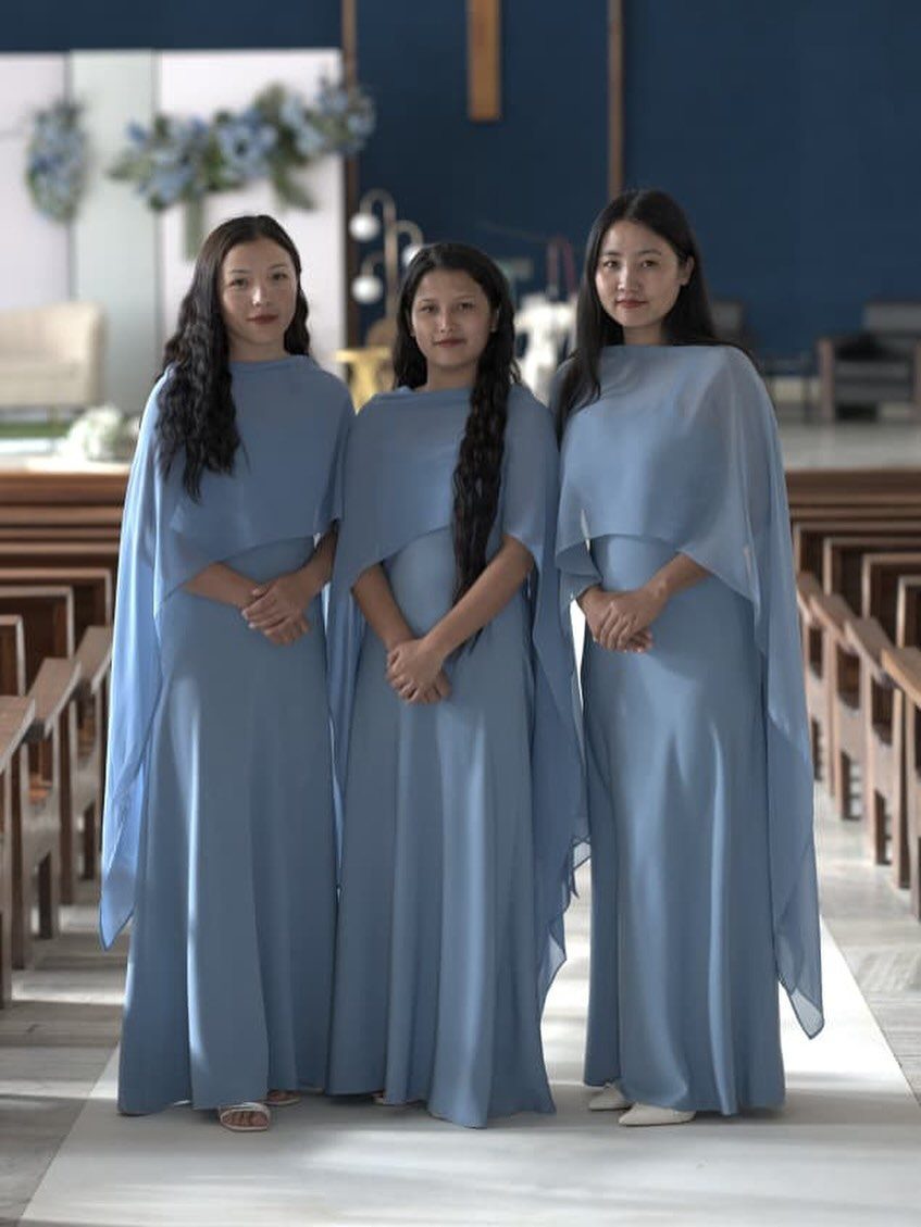 Three women wearing matching periwinkle blue bridesmaid dresses standing in a church aisle.